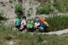 drei Kinder sitzen in einer Kiesgrube vor einem Feuchtbiotop und suchen nach Tiere