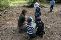 Kniende Waldführerin zeigt drei Kindern im Wald Kartenmaterial