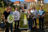 7 Personen stehen im Garten vor einem Plakat
