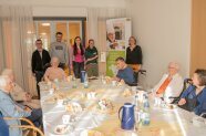 Eine Gruppe von Menschen und Senioren sitzen und stehen um einen Tisch