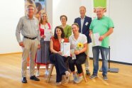 7 Personen stehen zusammen, 2 halten eine Urkunde in der Hand