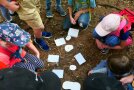 Kinder hocken im Kreis auf Waldboden und haben in der Mitte verschiedene Tierspuren vor sich