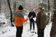 Eine Försterin steht im winterlichen Wald mit zwei Herren die auf Klemmbrettern schreiben