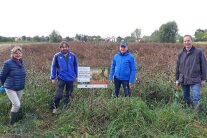 Vier Personen stehen neben Schild an Feldrand