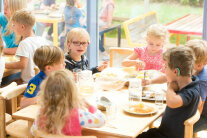 Kita Kinder sitzen zusammen am Esstisch und essen.