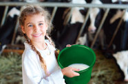 Mädchen im Kuhstall hält Eimer mit Milch hoch und lacht. © Pavel Losevsky - fotolia.com
